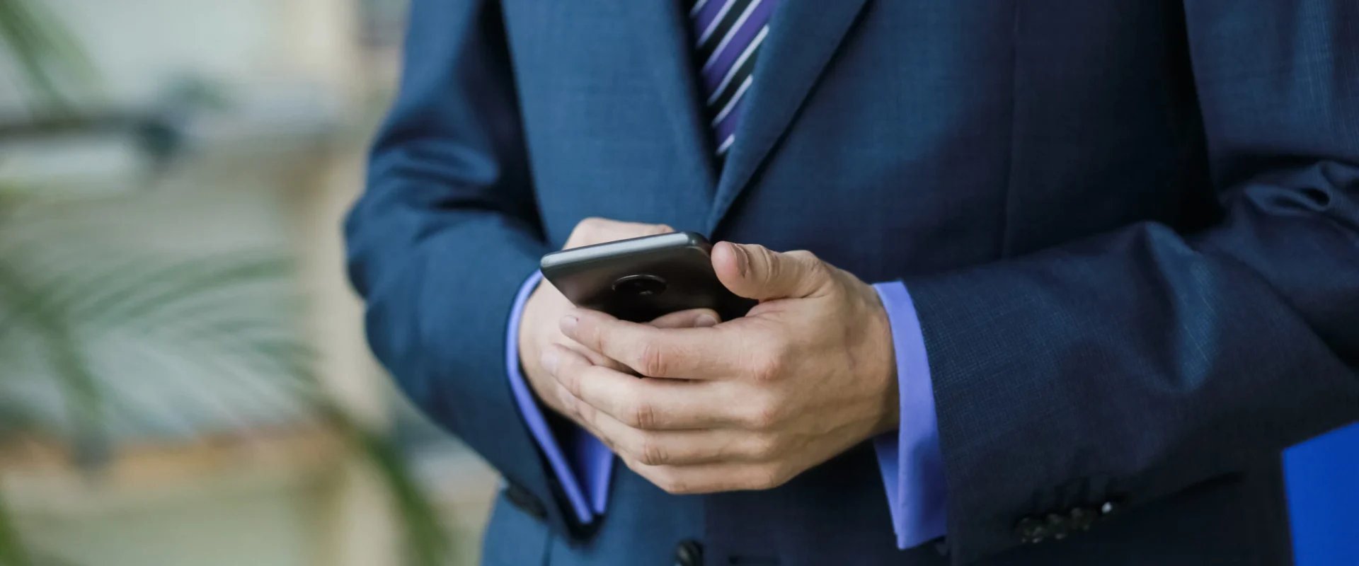 man-office-worker-suit-with-smartphone-near-window-palm-trees-scaled